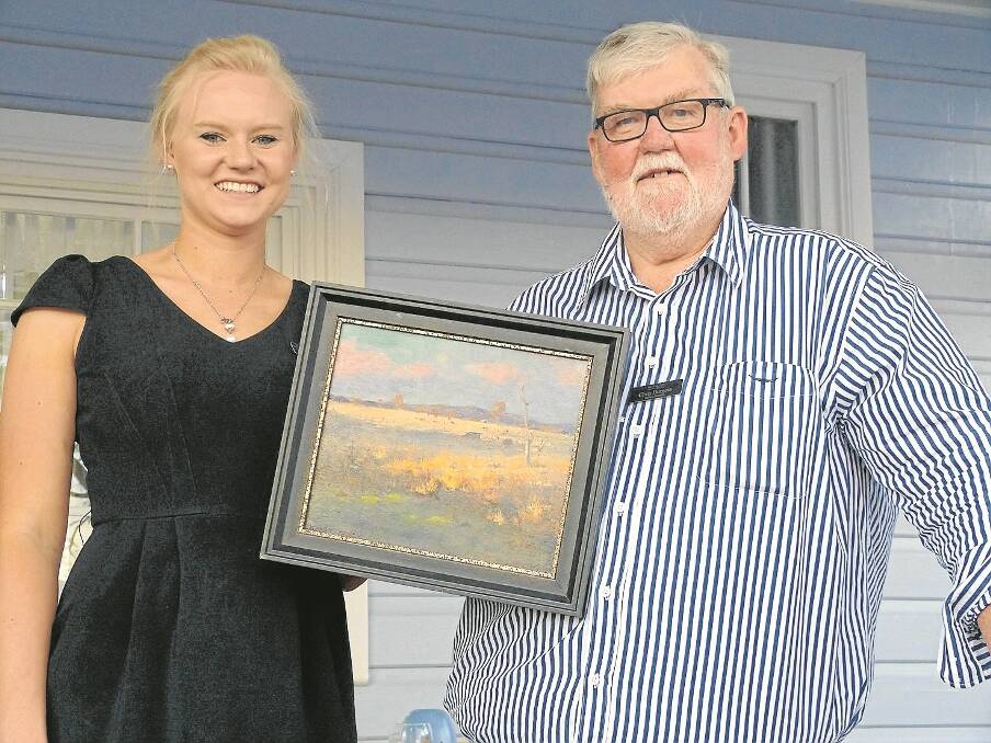 work of Art Community Gallery staff member Jen Hutchison and owner Chris Burgess display the auction piece.