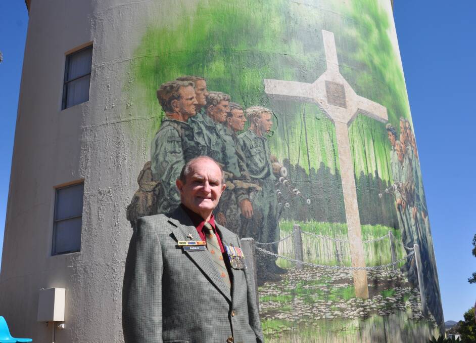 Neil Rankin standing in front of an image of his younger self in the Long Tan mural on the Gunnedah Water Tower Museum. Names of the Honour Guard at Long Tan taken in 1969. Left side of mural: Sgt Neil Rankin, Cpl George Richardson, Cpl William Akell, Cpl Brian Halls, Cpl Bill Roche and piper Cpl Gordon Black. Right side of mural: Cpl William O'Rourke, Sgt John Beere, Cpl Brian Riley, L'cpl Malcolm Campbell, Cpl Richard Brown and piper Cpl David Newlands.