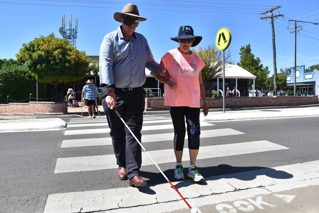 Gunnedah Shire Council’s Andrew Johns dons goggles and uses a cane to navigate the crossing in Elgin Street. He is aided by deputy mayor Gae Swain.