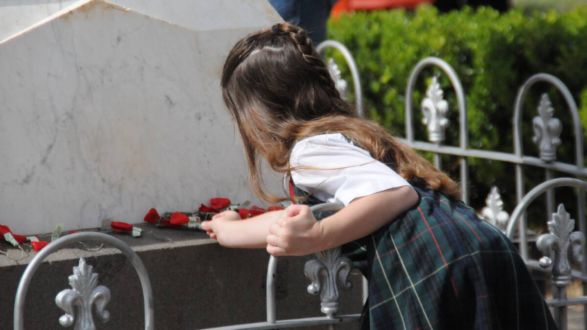 A young girl lays a poppy.